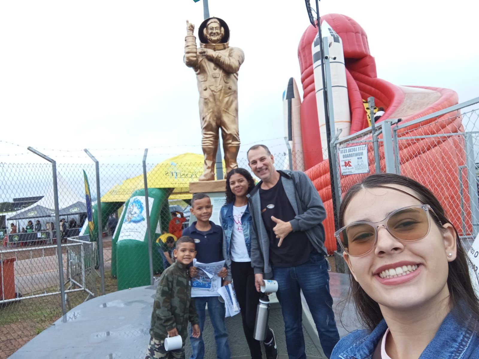 Família visitando o Arraiá Aéreo 2026 em Bauru ao lado da estátua do astronauta